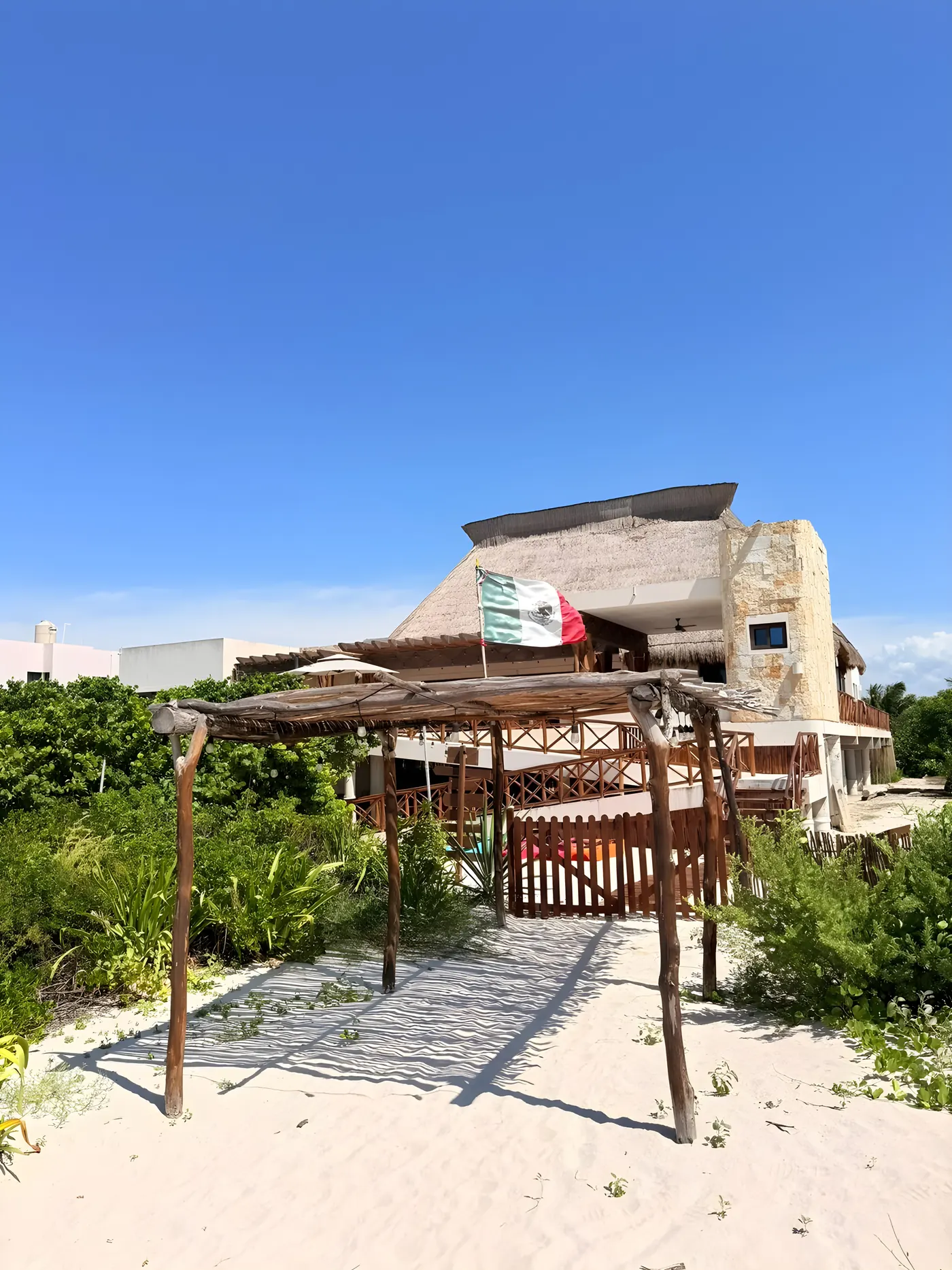 Casa María vista desde la playa, con pérgola de madera sobre la arena